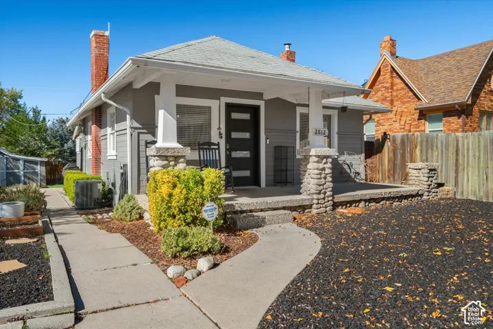 Bungalow exterior featuring a covered front porch with stone-clad columns, dual brick chimneys, and a modern paneled front door