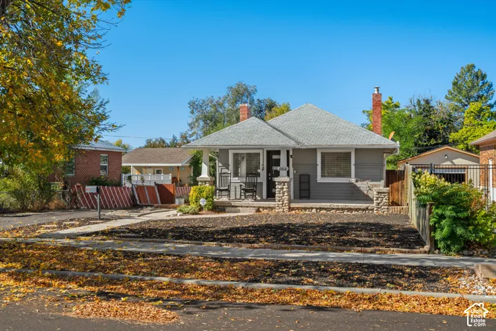 Single-story residence featuring a covered porch with stacked-stone pillar bases, two masonry chimneys, and horizontal siding