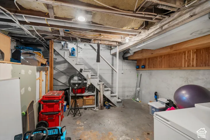 Unfinished utility space featuring concrete foundation walls, wood-paneled accent wall, open-joist ceiling, and built-in staircase