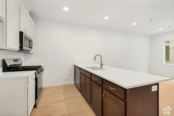 Kitchen featuring white upper cabinetry, brown lower cabinetry, stone-finish countertops, stainless steel appliances, and wood-finish flooring