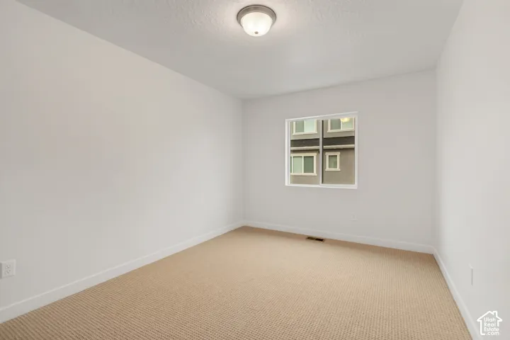 Neutral-toned interior space featuring light-colored wall-to-wall carpeting, crisp white walls, and a center-mounted ceiling light fixture