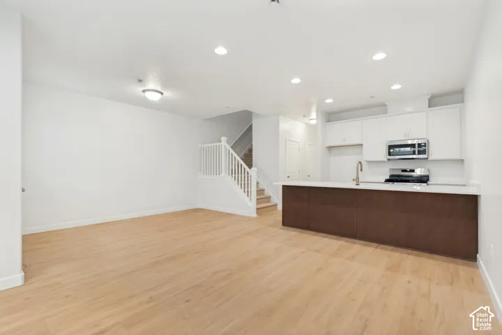 Open floor plan featuring wood-finish flooring, recessed lighting, white cabinetry, quartz-style countertops, and a staircase with white wood balusters