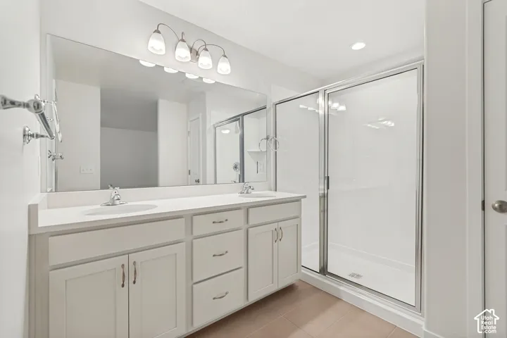 Double vanity featuring white cabinetry, a solid-surface countertop with dual undermount sinks, a full-width mirror, and a glass-enclosed shower with chrome fixtures