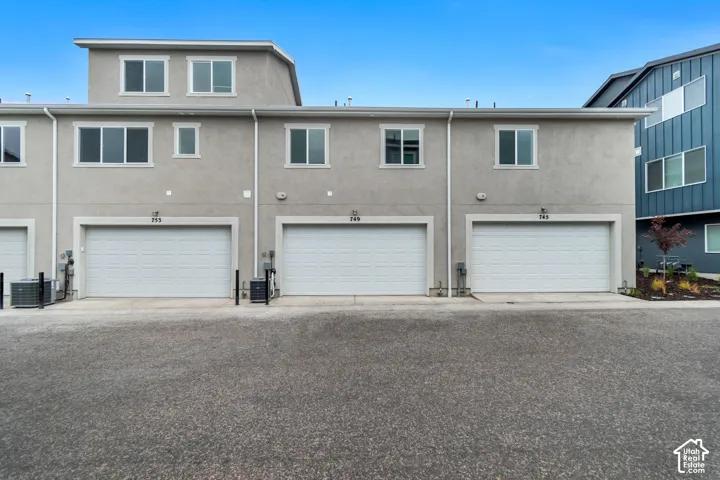 Multi-unit exterior featuring a smooth stucco facade, three private garages with sectional roll-up doors, multi-level construction, and asphalt paving