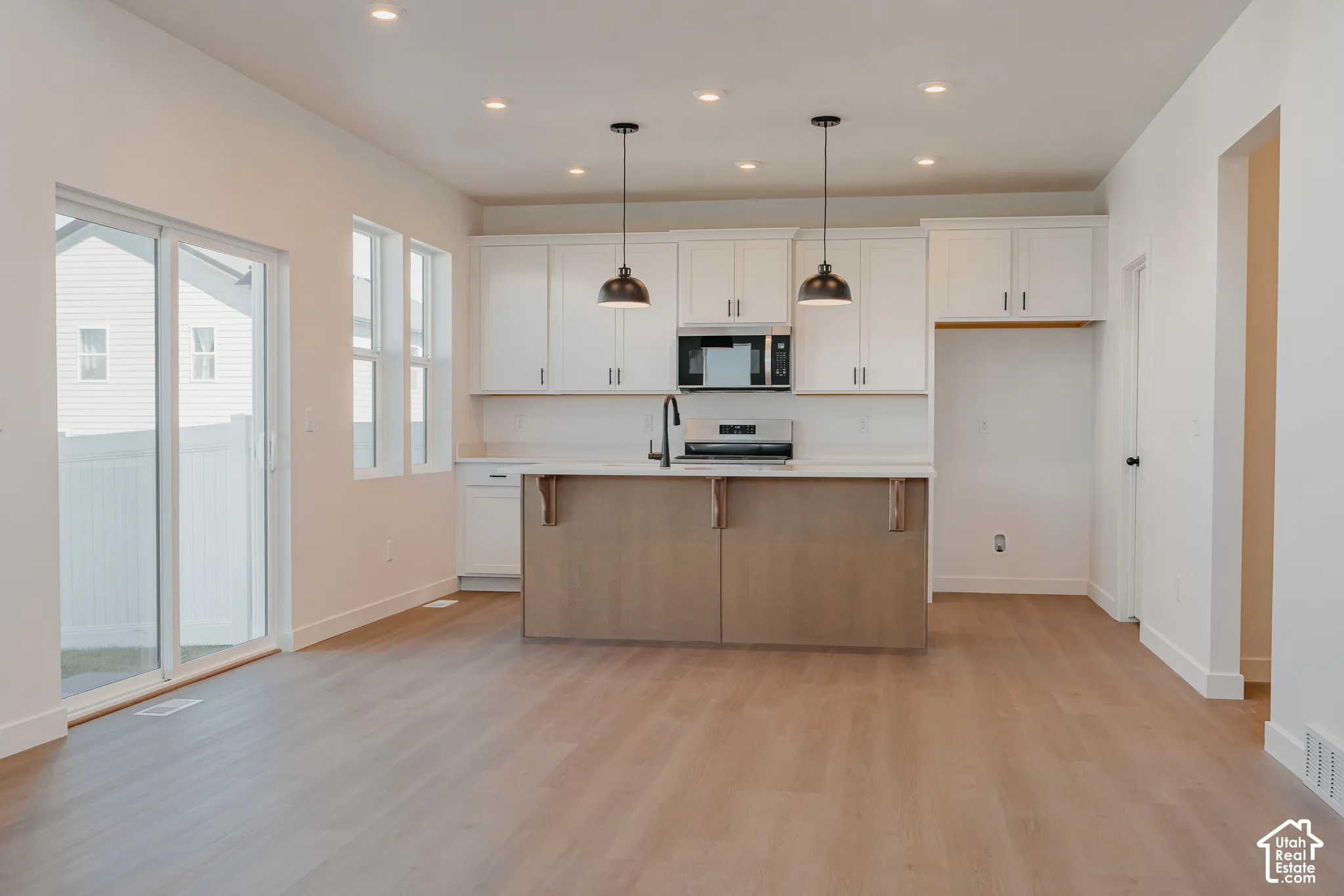 Kitchen featuring white cabinetry, a center island with a wood-finish base, quartz countertops, dual pendant lighting, and recessed ceiling lights