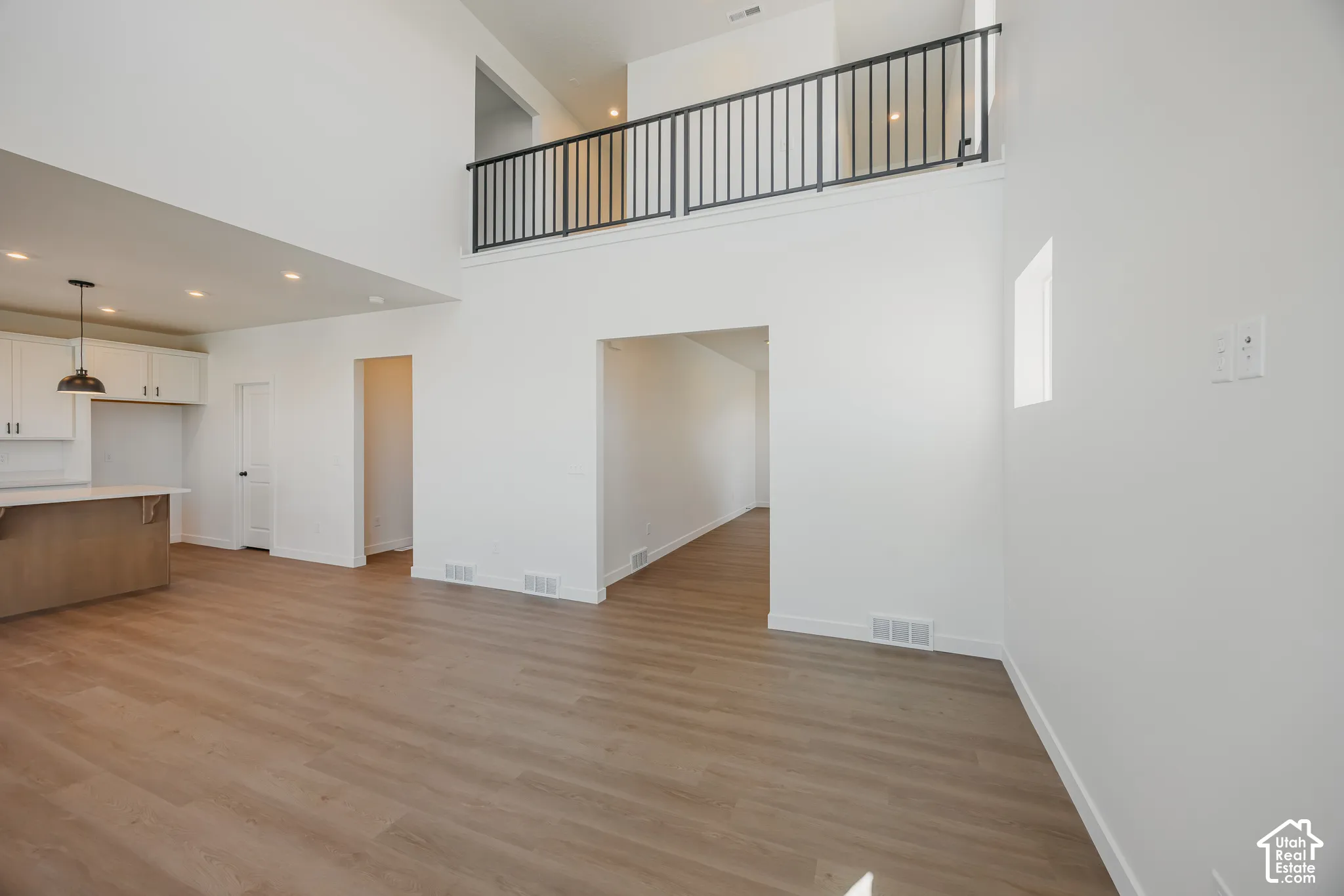 Double-height ceiling featuring a balcony with a black metal railing, wood-finish flooring, recessed lighting, and a kitchen island with built-in cabinetry