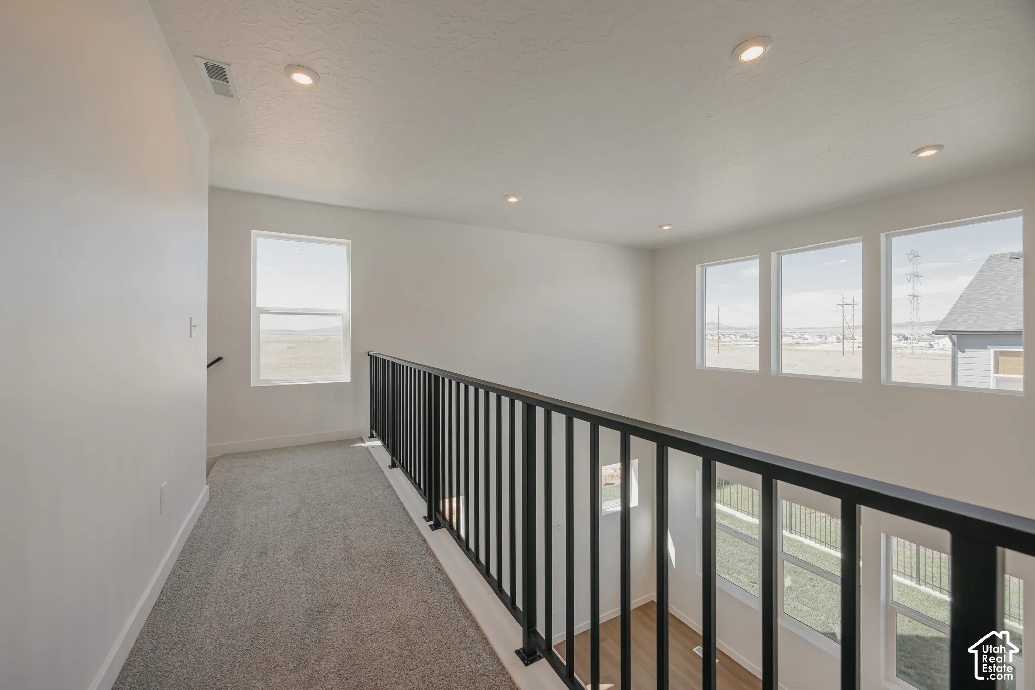 Open landing featuring wall-to-wall carpeting, black metal baluster railing, recessed lighting, and expansive windows