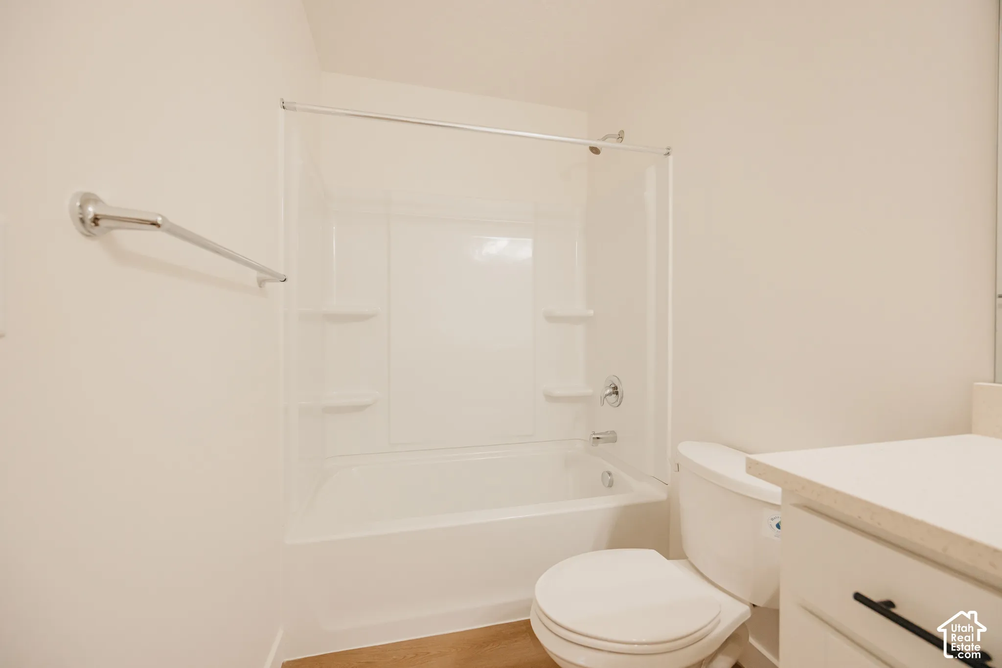 Bathroom featuring a white tub-and-shower combination with integrated shelving, chrome shower fixtures, a chrome towel bar, and a vanity with matte black hardware