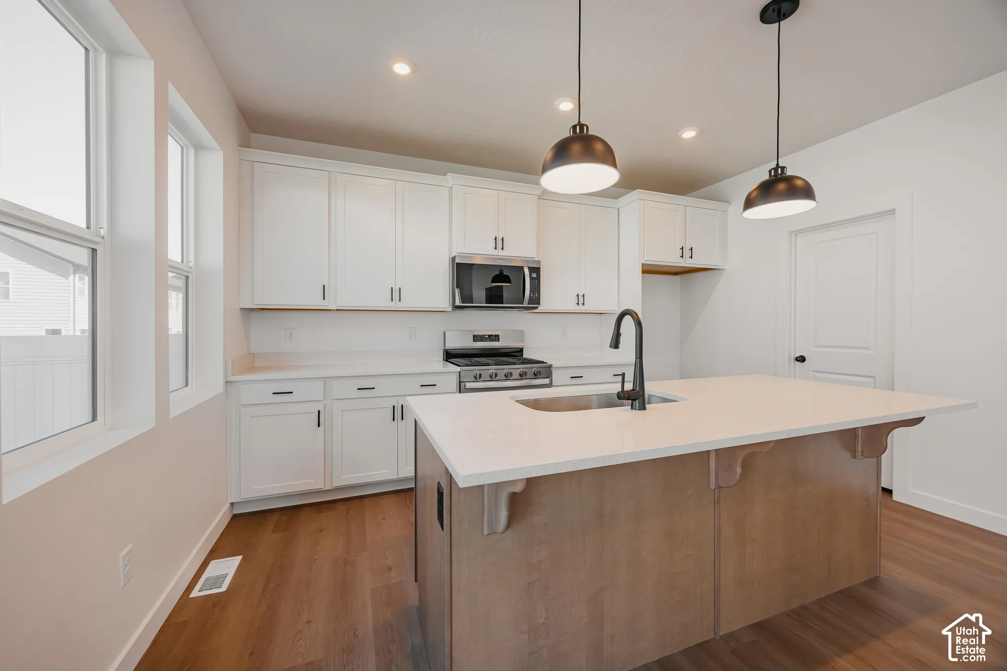 Kitchen featuring white shaker-style cabinetry, quartz countertops, a central island with wood-finish base, stainless steel gas range with built-in microwave, and matte black pendant lighting