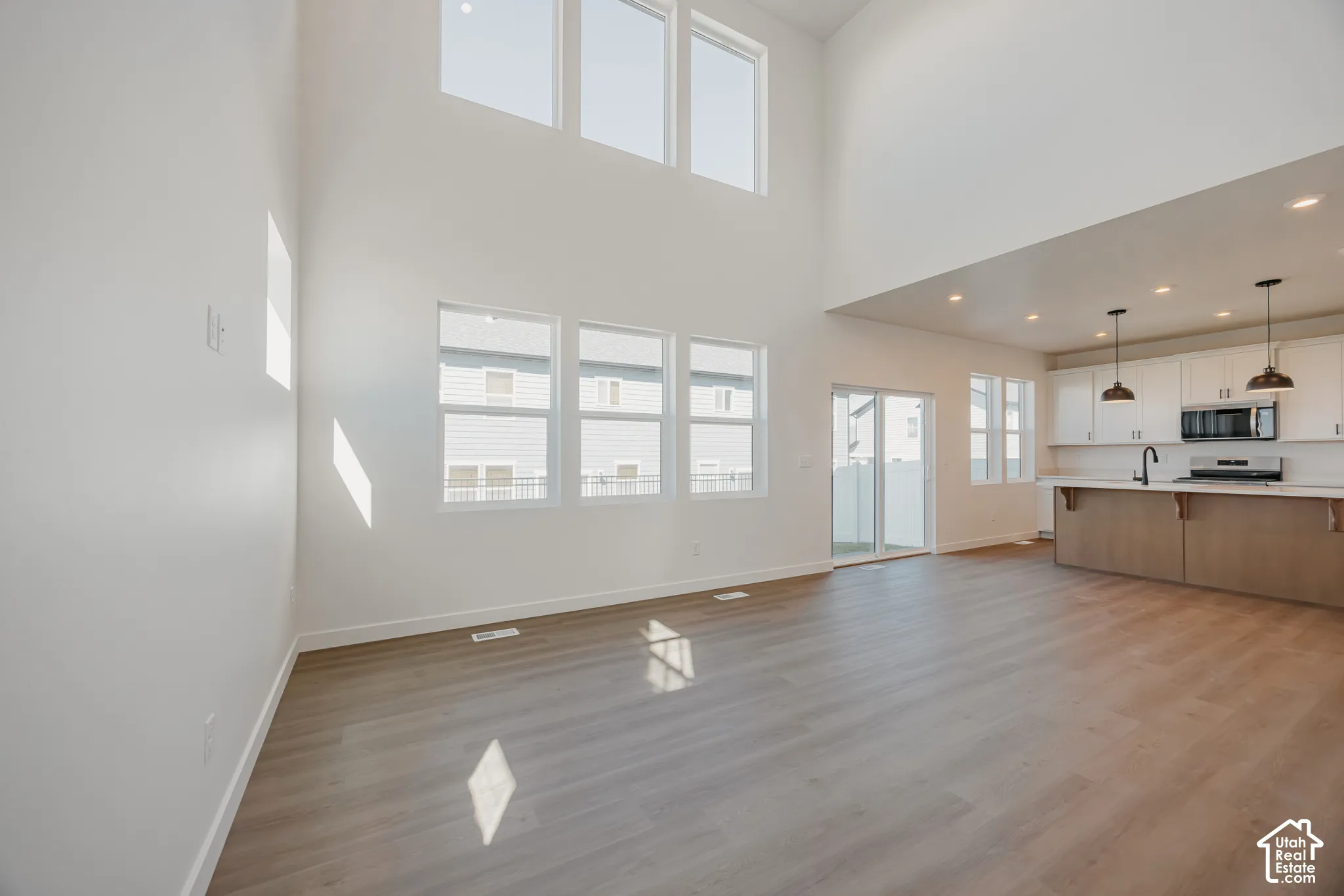 Double-height vaulted ceilings featuring expansive windows, wood-finish flooring, kitchen island with built-in cabinetry, and recessed lighting