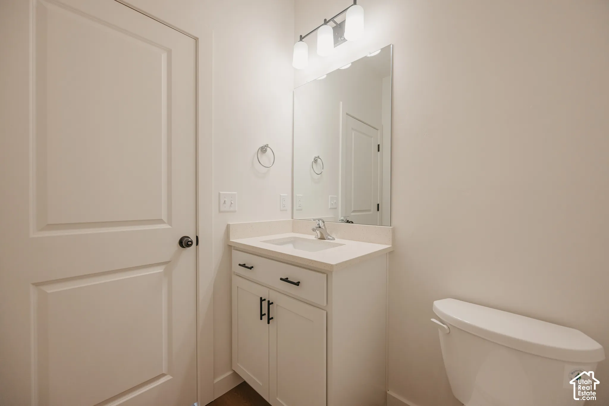 Bathroom featuring a white vanity cabinet with matte black hardware, a solid surface countertop with an integrated sink, a large frameless mirror, and a multi-bulb light fixture