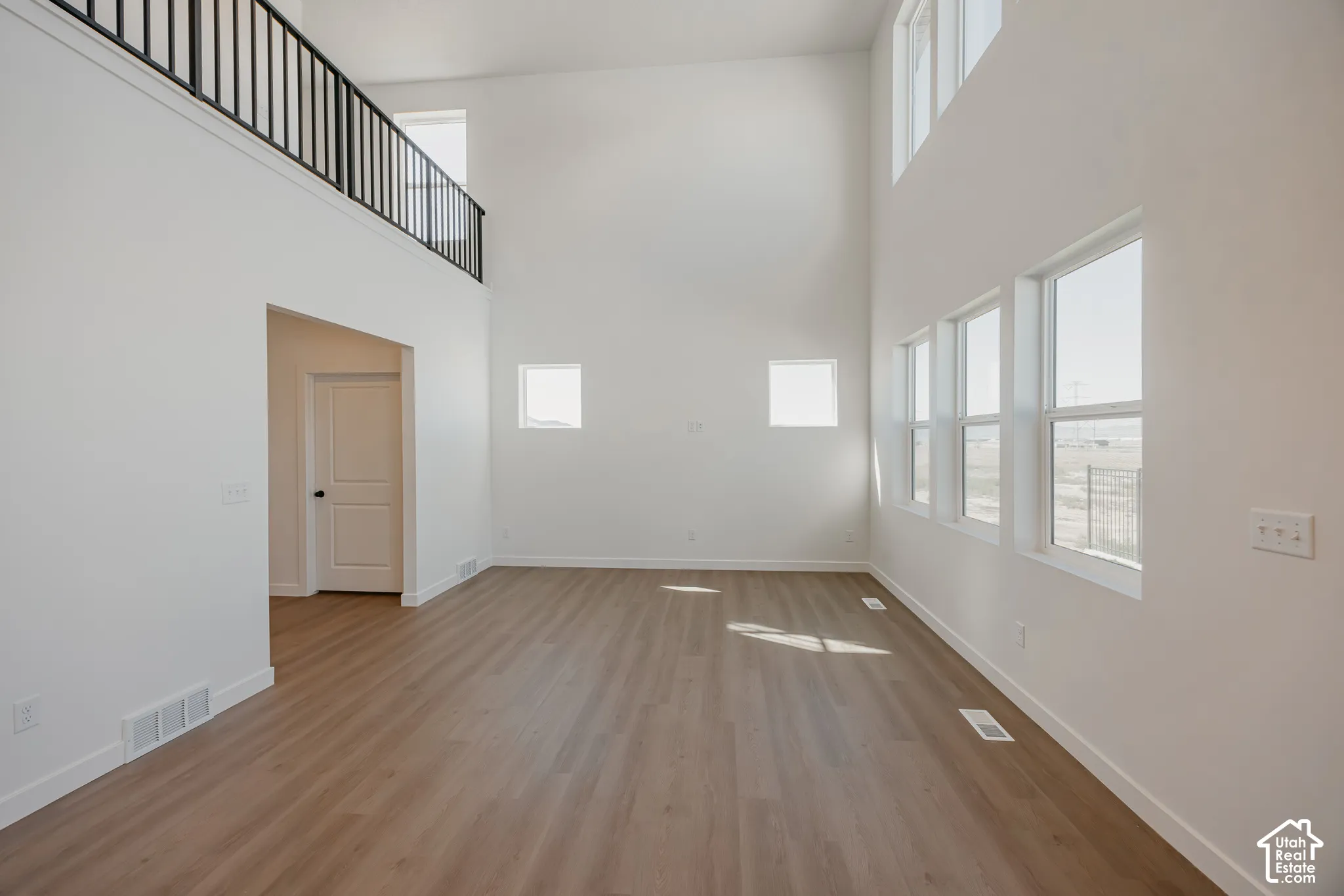 High-ceiling interior featuring wood-finish flooring, metal railing, and multiple large windows