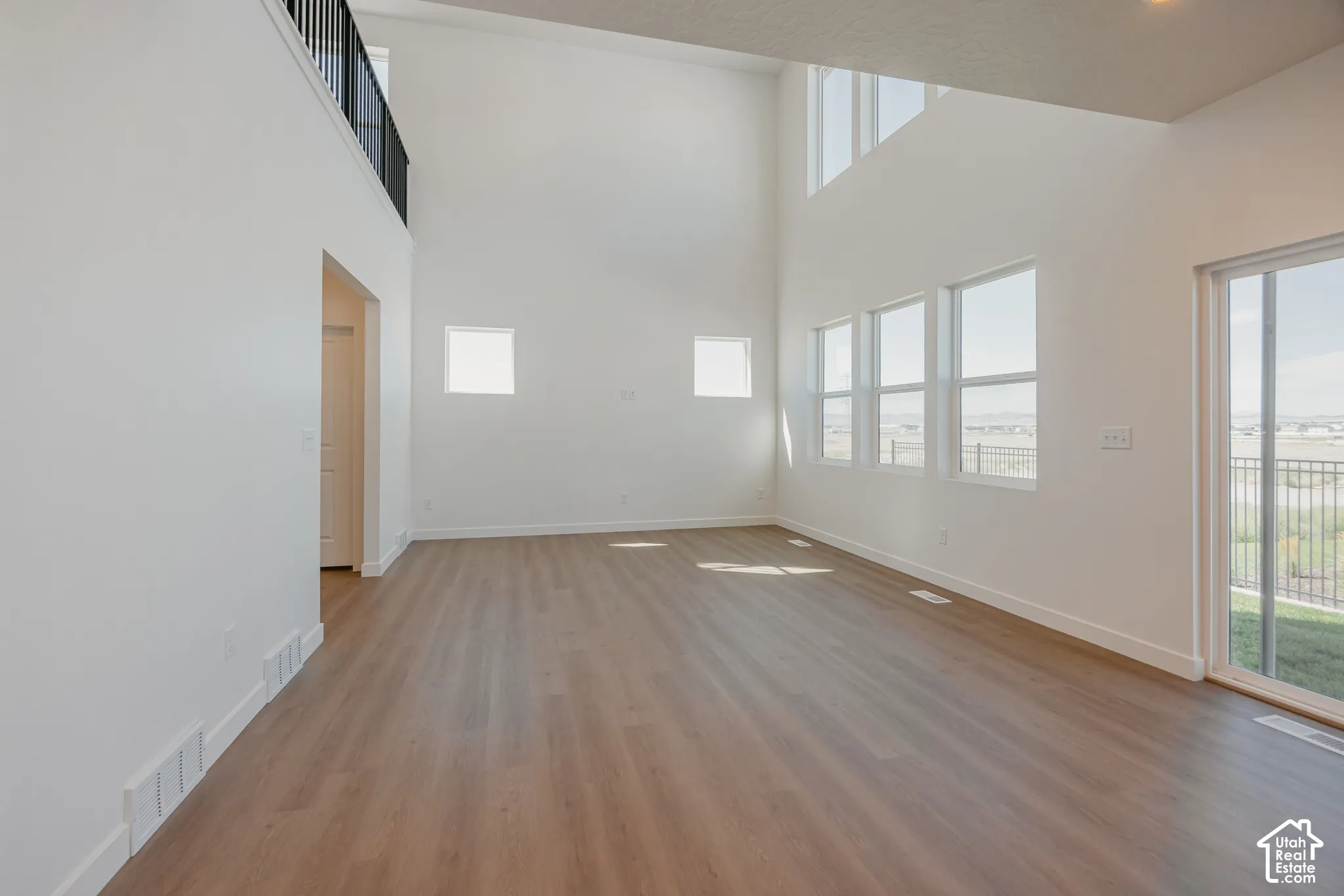 Expansive room featuring double-height ceilings, wood-finish flooring, large multi-pane windows, and a metal-railed interior balcony