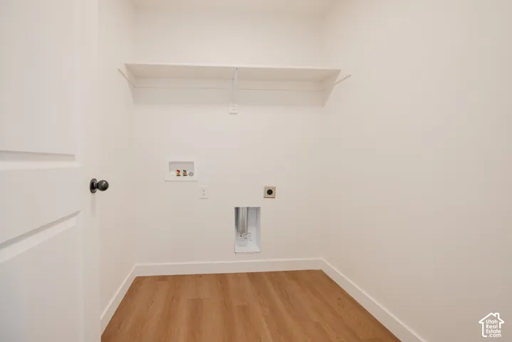 Utility closet featuring wood-finish flooring, a wall-mounted shelving unit, and dedicated hookups for laundry appliances