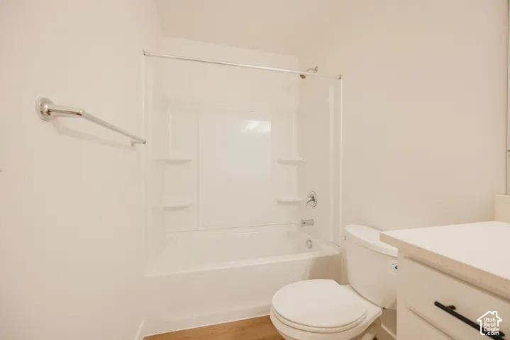 Bathroom featuring a white tub-and-shower combination with integrated shelving, chrome shower fixtures, a chrome towel bar, and a vanity with matte black hardware