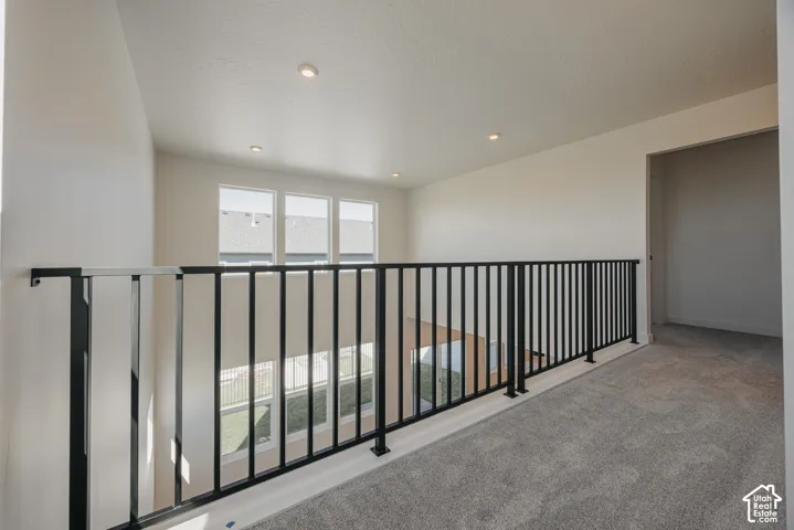 Landing area featuring neutral carpeting, recessed ceiling lighting, and a black metal railing overlooking the lower level