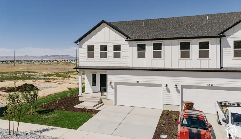Modern two-story exterior featuring white horizontal siding, vertical board-and-batten accents, dual-car garage, and asphalt shingle roof