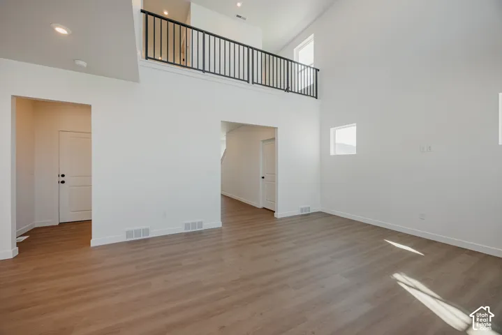 High-ceiling interior featuring a mezzanine level with black metal railings, wood-finish flooring, recessed lighting, and multi-panel interior doors