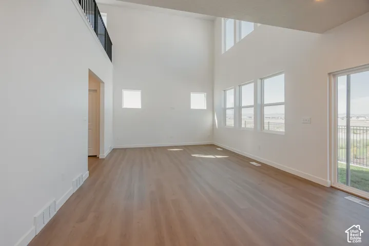 Expansive room featuring double-height ceilings, wood-finish flooring, large multi-pane windows, and a metal-railed interior balcony