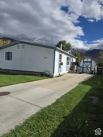 Single-level exterior featuring horizontal siding, a concrete driveway, a detached storage shed, and a mountain backdrop