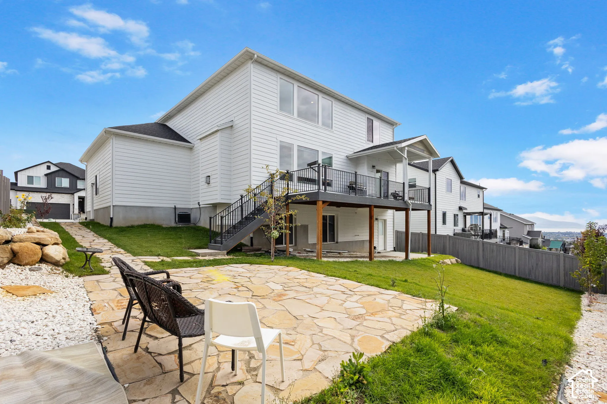 Two-story vinyl-sided exterior featuring an elevated deck with black metal railing, a covered patio area, and flagstone hardscaping