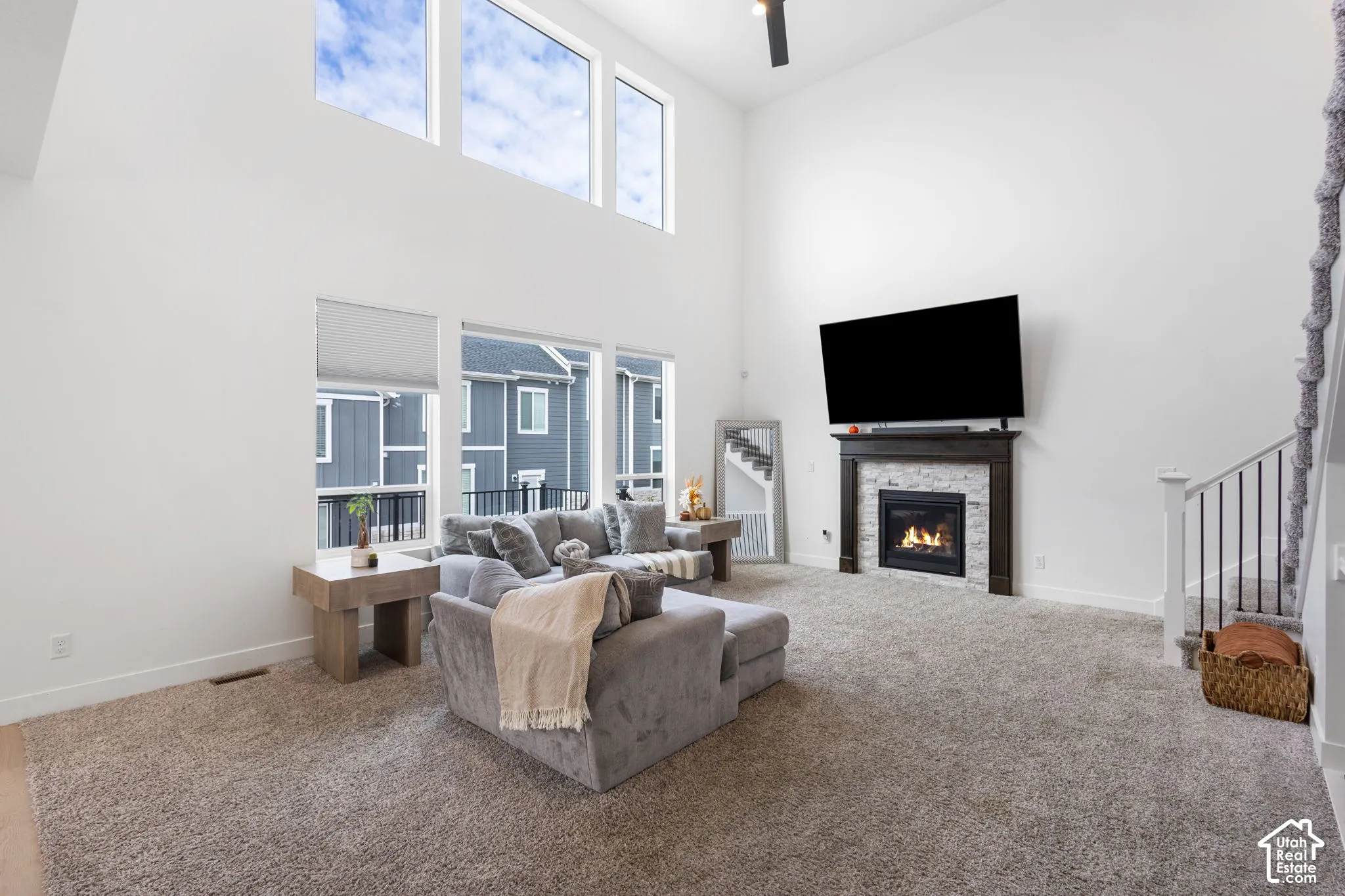 High-ceilinged living area featuring a floor-to-ceiling stone-surround fireplace with a wooden mantel, oversized windows, and a staircase with metal railings