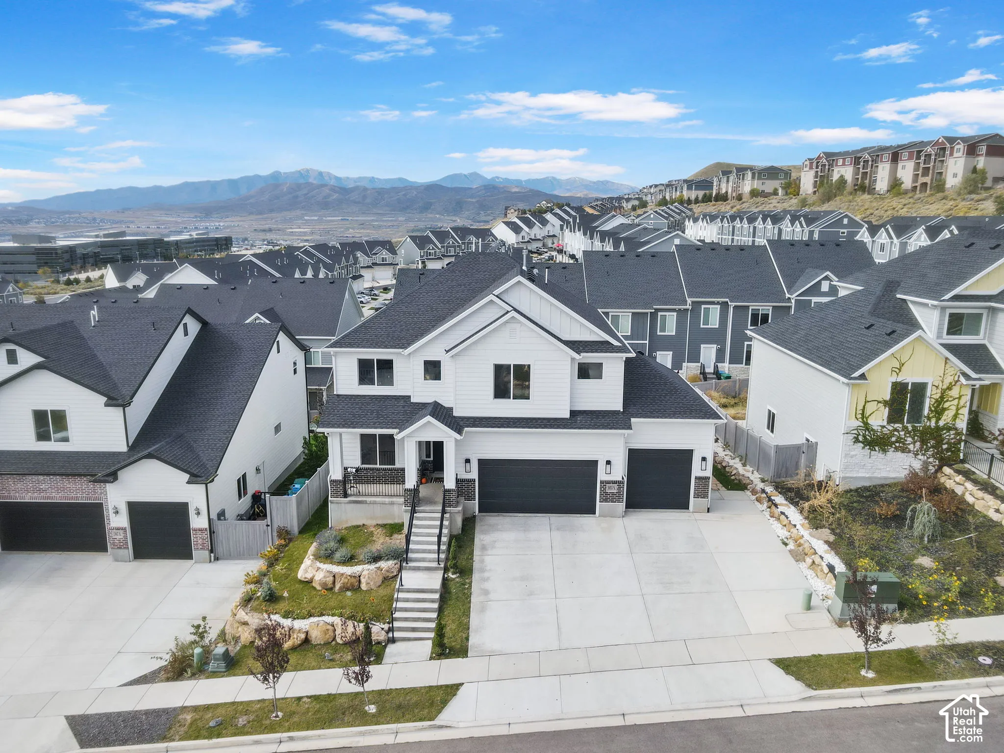 Two-story residence featuring white horizontal siding, dark shingled roof, three-car garage, concrete driveway, and stone-retained landscaping