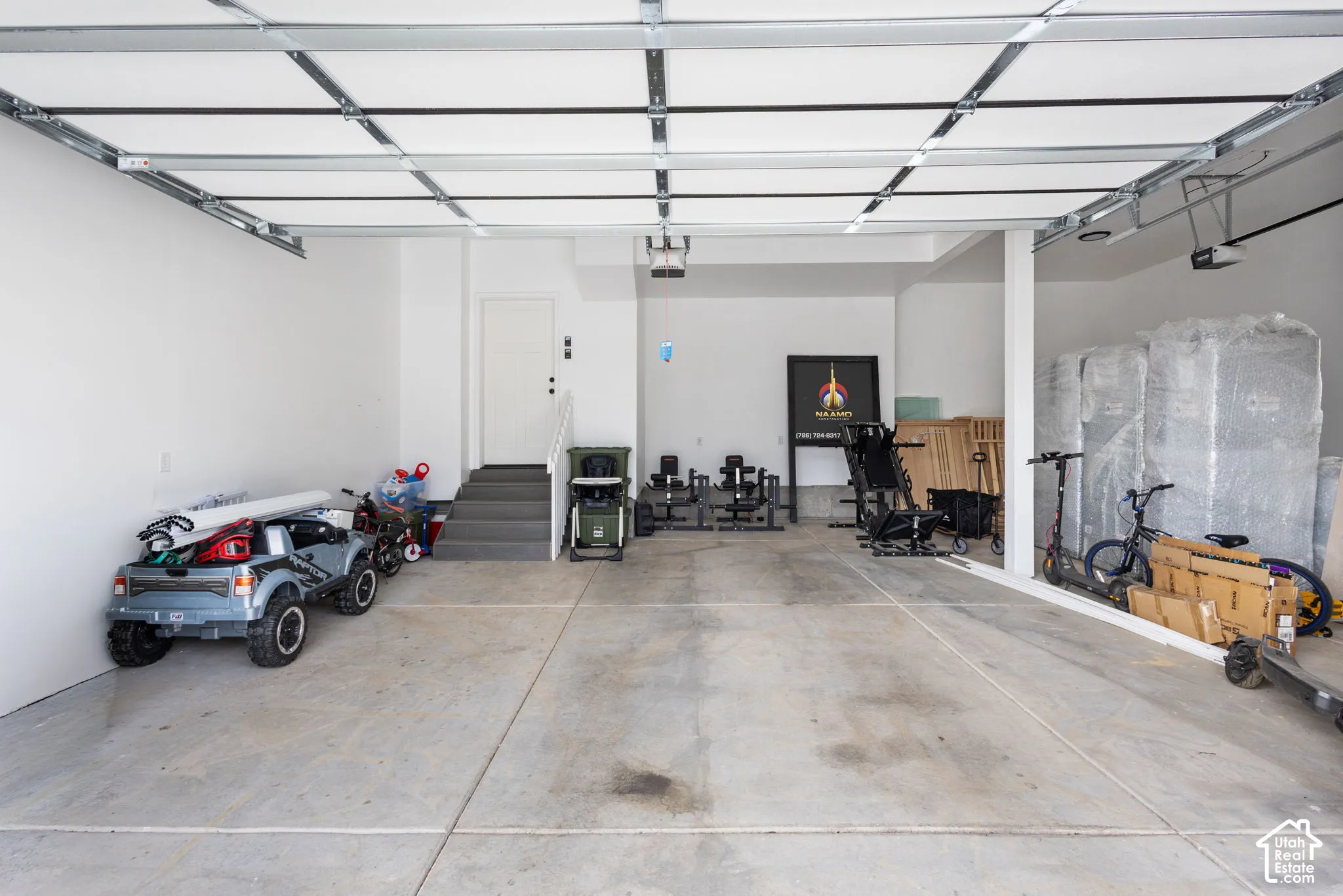 Attached garage featuring a concrete floor, high ceiling with exposed mechanical tracks, and interior access stairs