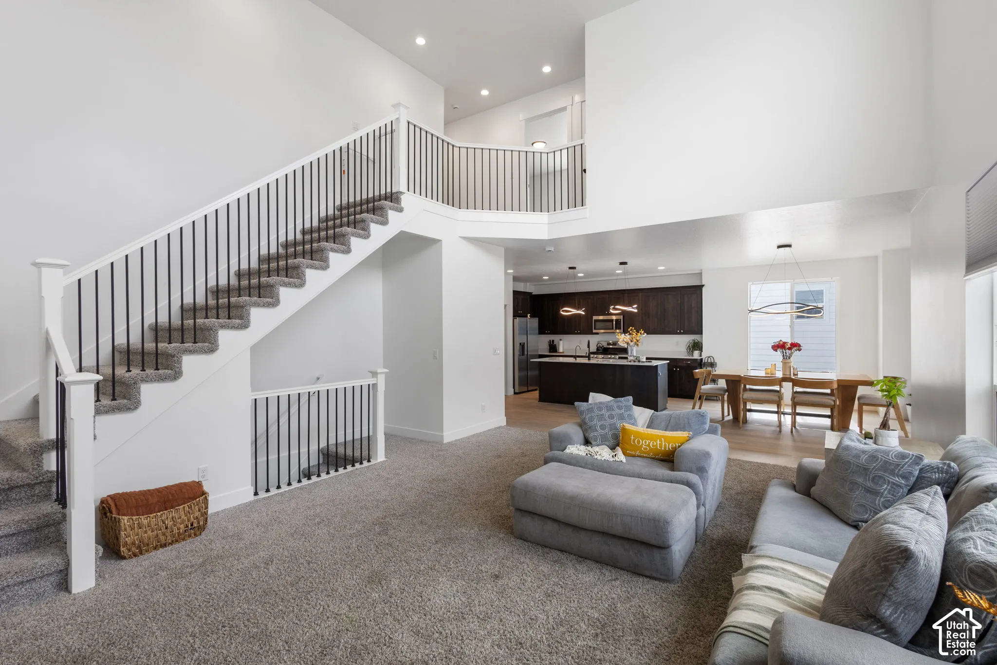 High ceilings, staircase with white railings and thin black balusters, recessed lighting, and kitchen with dark-finish cabinetry and a central island