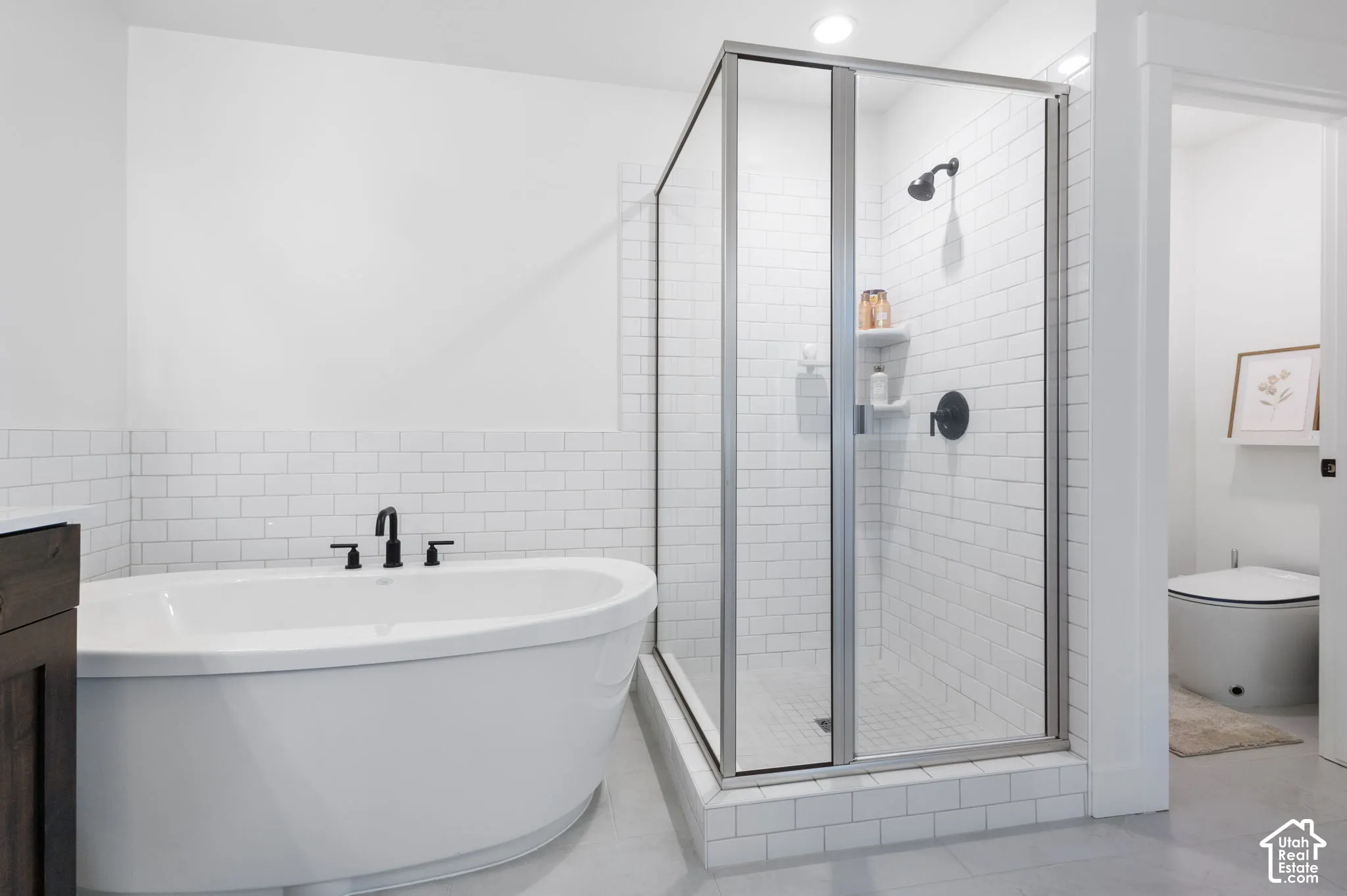 Freestanding soaking tub with matte black fixtures, glass-enclosed shower with subway tile surround, and integrated tile shelving