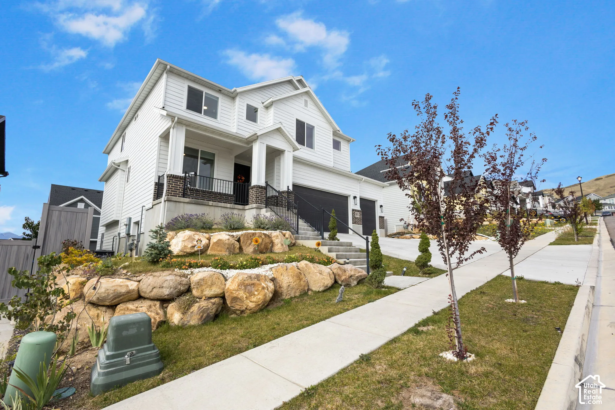 Two-story exterior featuring white horizontal siding, a multi-car garage, stone-accented front porch columns, and decorative boulder retaining walls