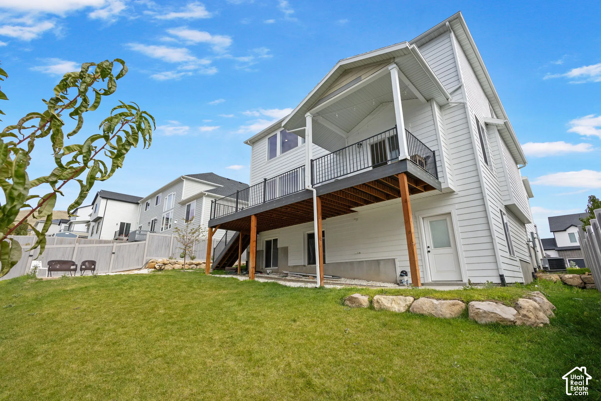 Two-story home with horizontal siding, elevated rear deck with metal railing, covered patio space, and tiered rock landscaping