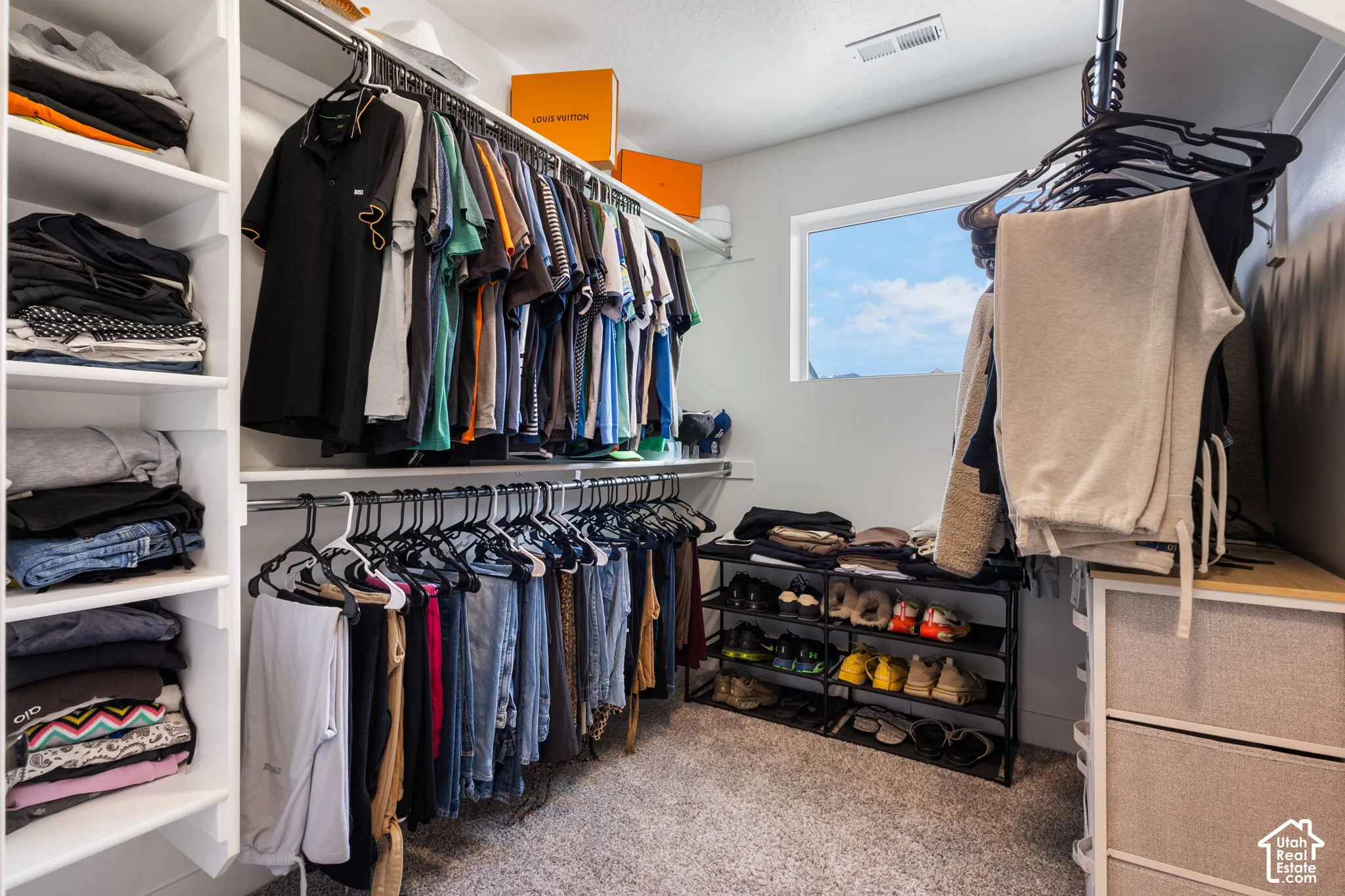 Walk-in closet featuring floor-to-ceiling built-in shelving, multi-level hanging rods, and a window providing natural light