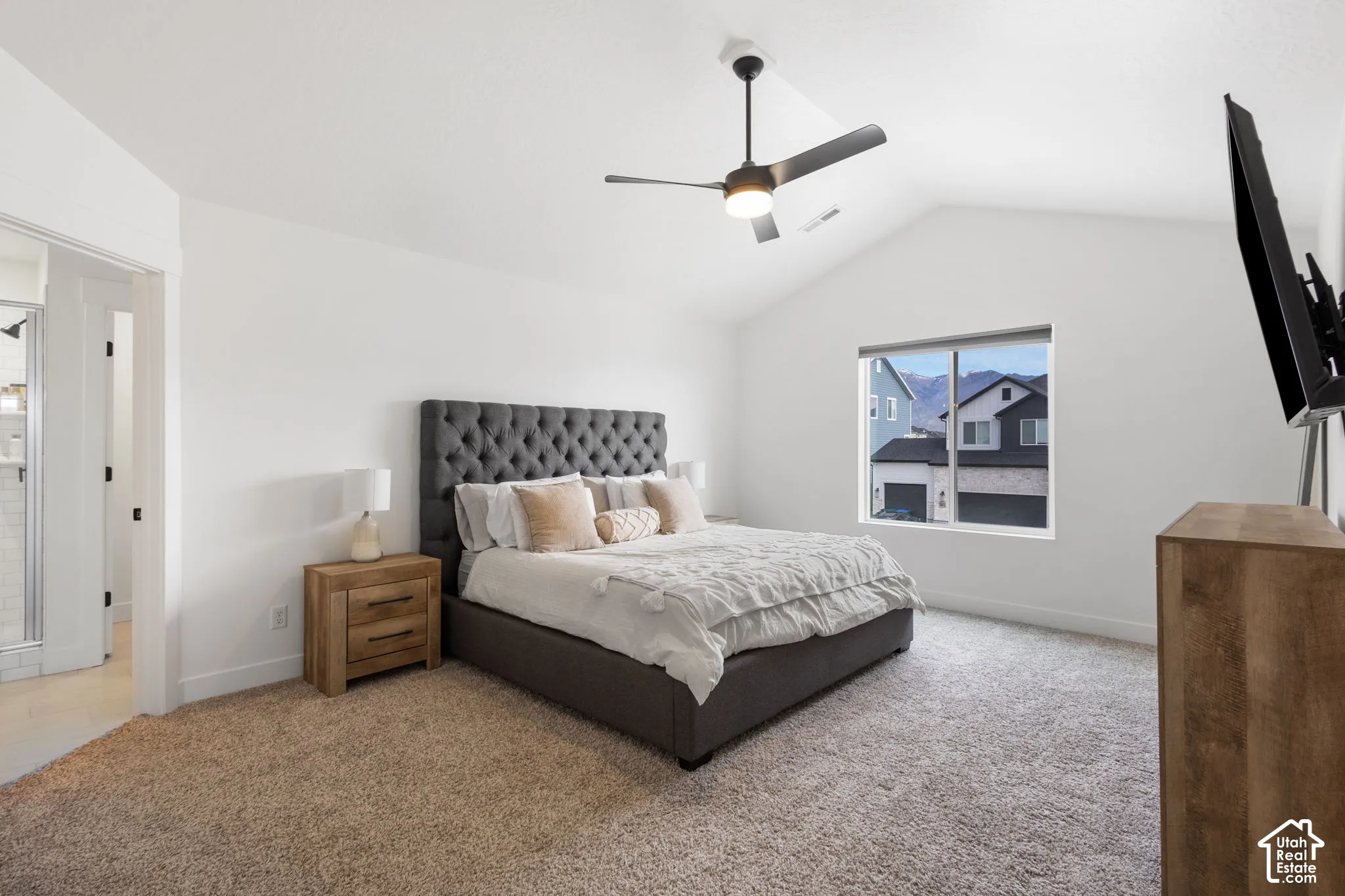 Vaulted ceiling featuring a central light-integrated ceiling fan, neutral carpeting, and a large window showcasing a mountain backdrop