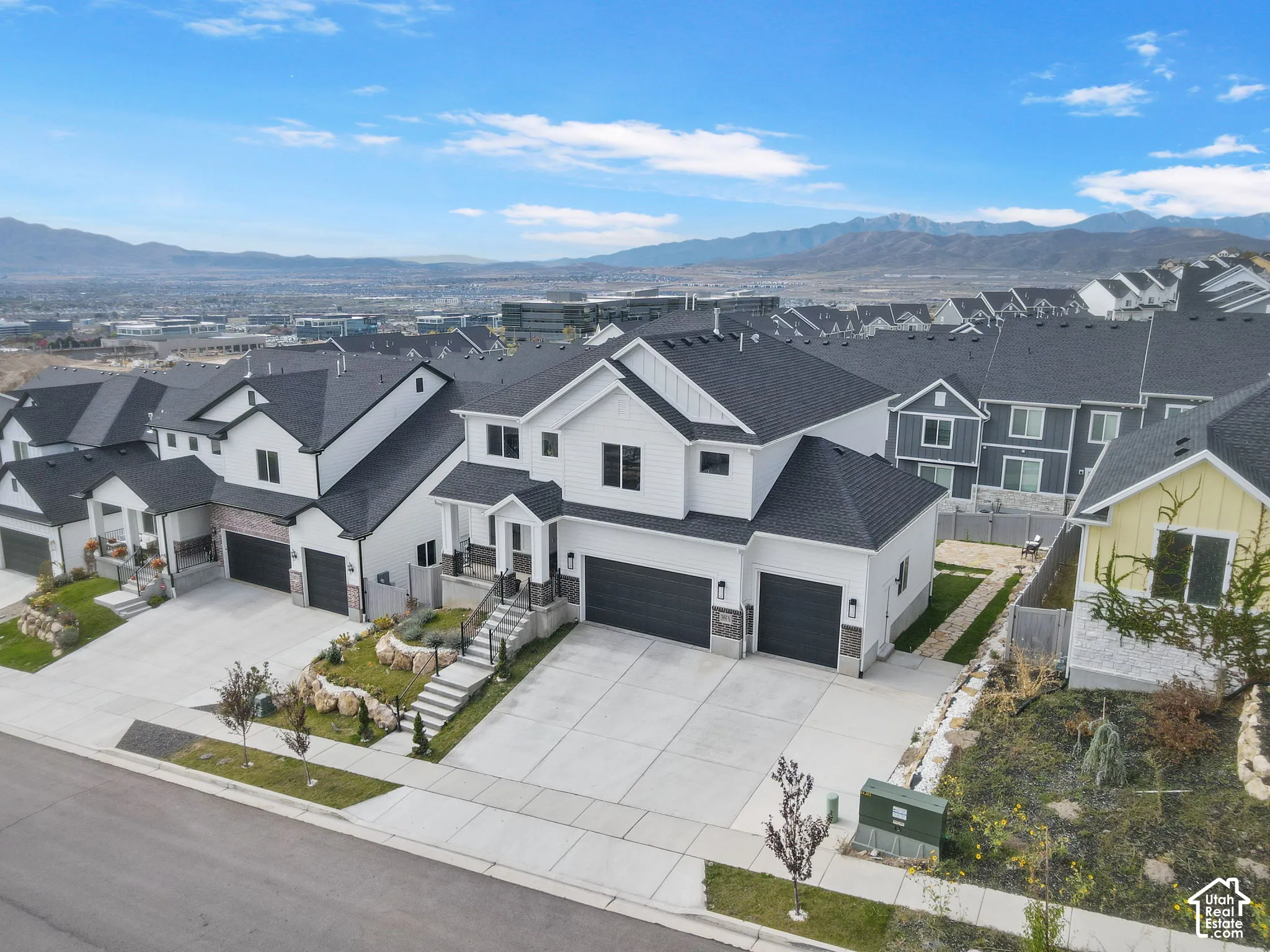 Two-story residence featuring a white exterior, attached three-car garage, concrete driveway, stone foundation accents, and mountain backdrop