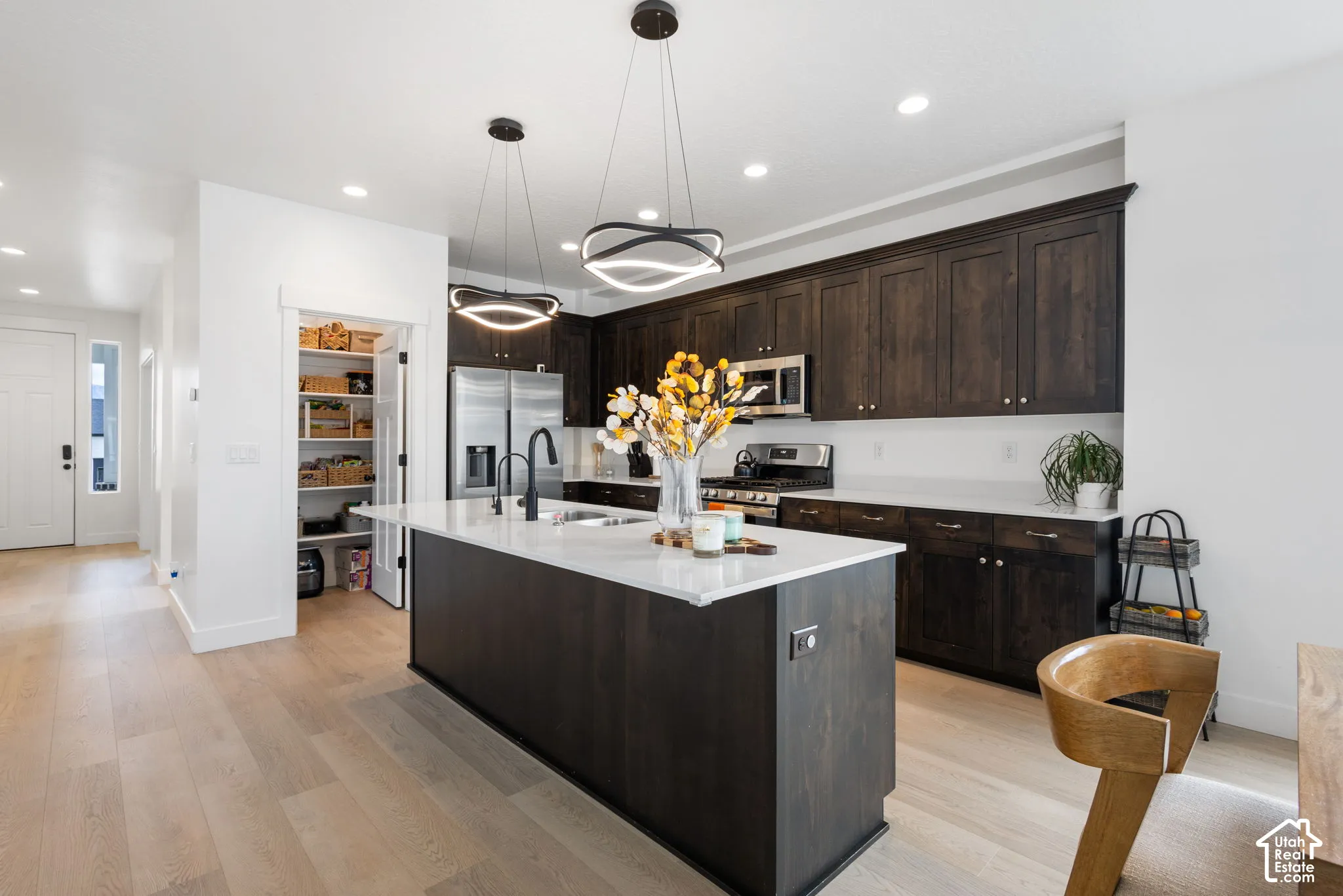 Kitchen featuring dark wood-finish cabinetry, a center island with light-toned countertops, matte black plumbing fixtures, modern geometric pendant lighting, and an expansive walk-in pantry