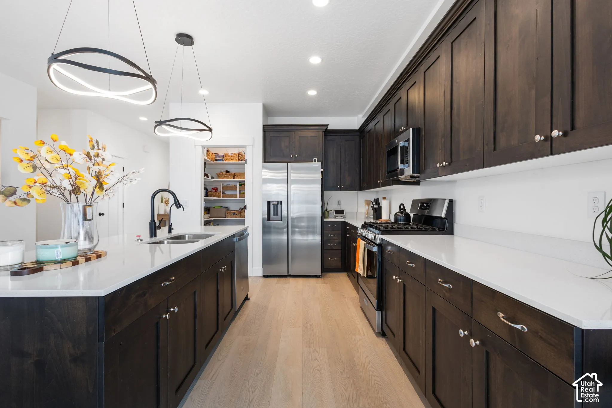 Kitchen featuring dark wood cabinetry, white countertops, stainless steel appliances, wood-finish flooring, and dual modern geometric pendant lights