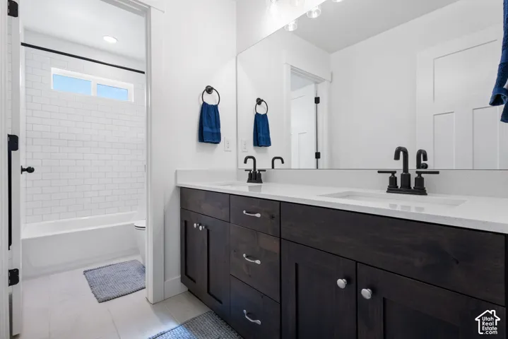 Dual-sink vanity with dark-finish cabinetry, light stone-composite countertop, matte black fixtures, and full-width vanity mirror