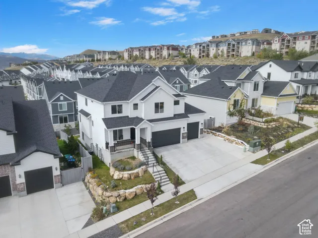 Two-story residence featuring white horizontal siding, a multi-gabled dark asphalt shingle roof, a two-car garage, and tiered stone retaining walls
