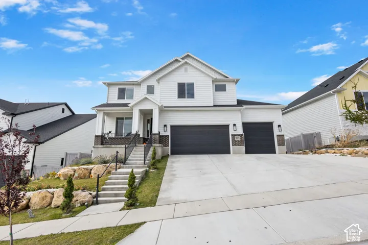 Two-story residence featuring white horizontal siding, dark brick veneer accents, a three-car garage, and concrete hardscaping with stone retaining walls