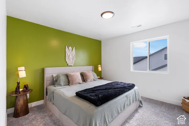 Bedroom featuring a prominent green accent wall, neutral carpeting, and a flush-mount ceiling light
