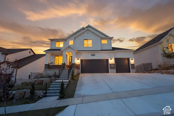 Two-story residence featuring horizontal siding, brick masonry detailing, a concrete driveway, a three-car garage, and a concrete staircase leading to a covered front porch