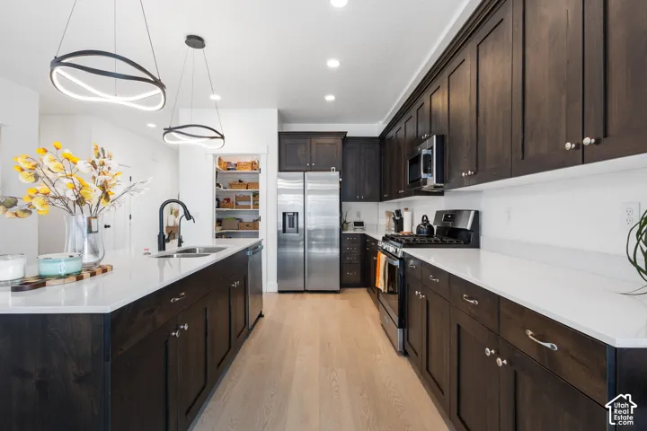 Kitchen featuring dark wood cabinetry, white countertops, stainless steel appliances, wood-finish flooring, and dual modern geometric pendant lights