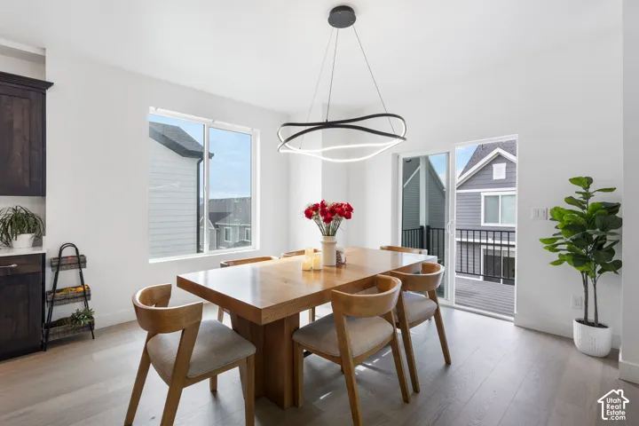 Wood-finish flooring, matte black sculptural LED pendant light, and sliding glass door leading to a railed balcony