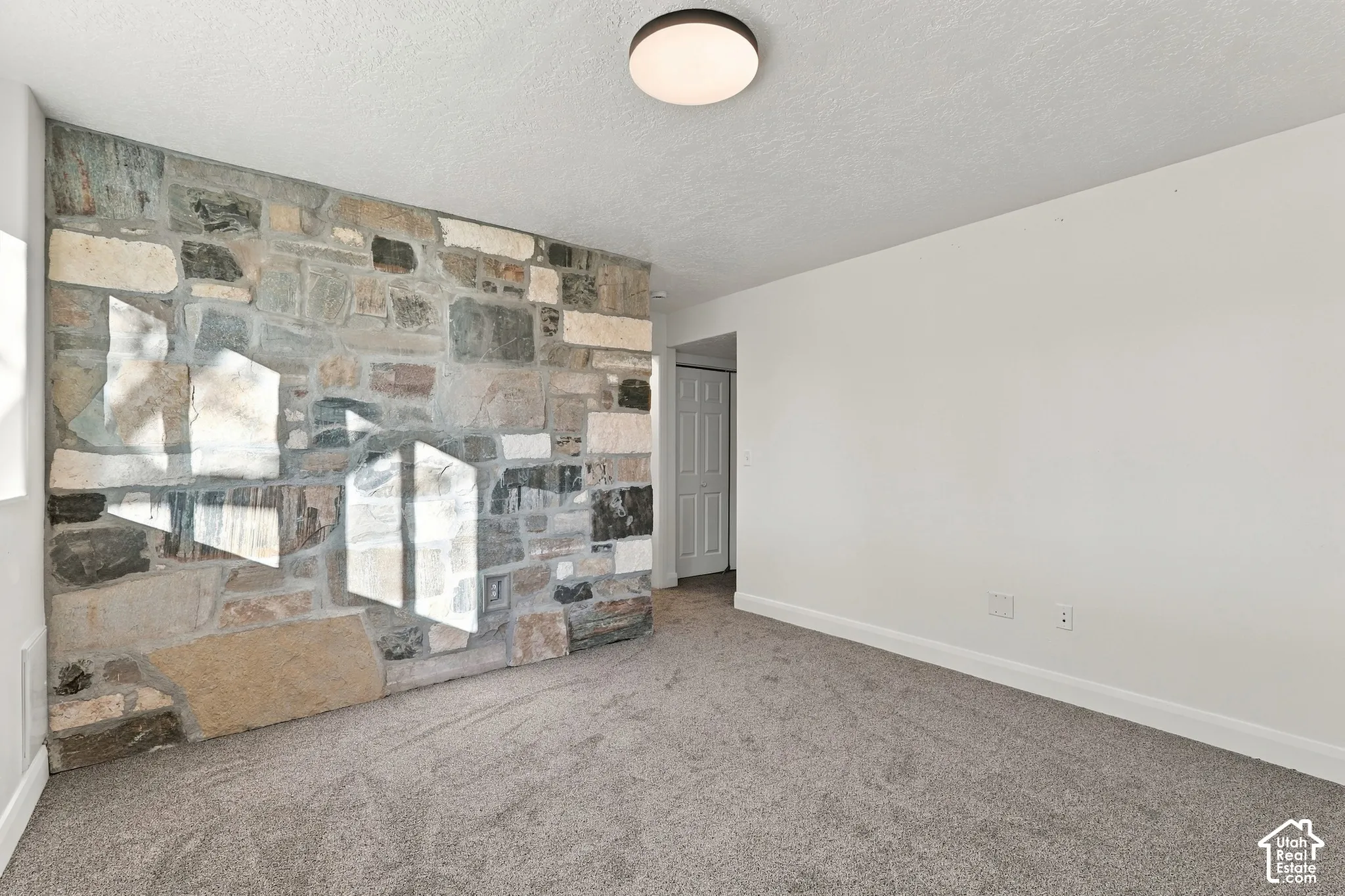 Room featuring a multi-tonal stone accent wall, neutral carpeting, and a flush-mount circular ceiling light fixture