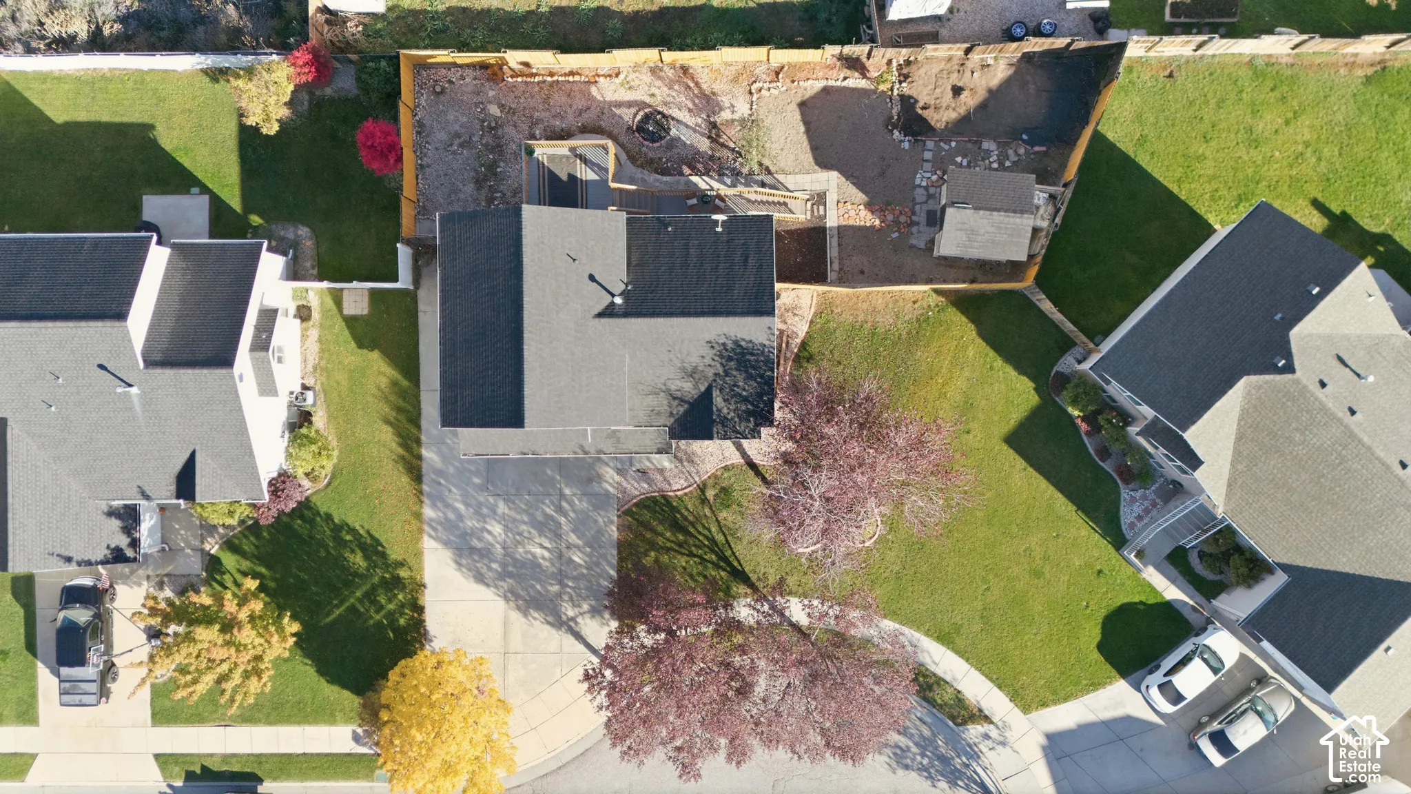 Aerial perspective featuring a residential lot with a concrete driveway, a rear yard area with stone hardscaping, and perimeter wood fencing