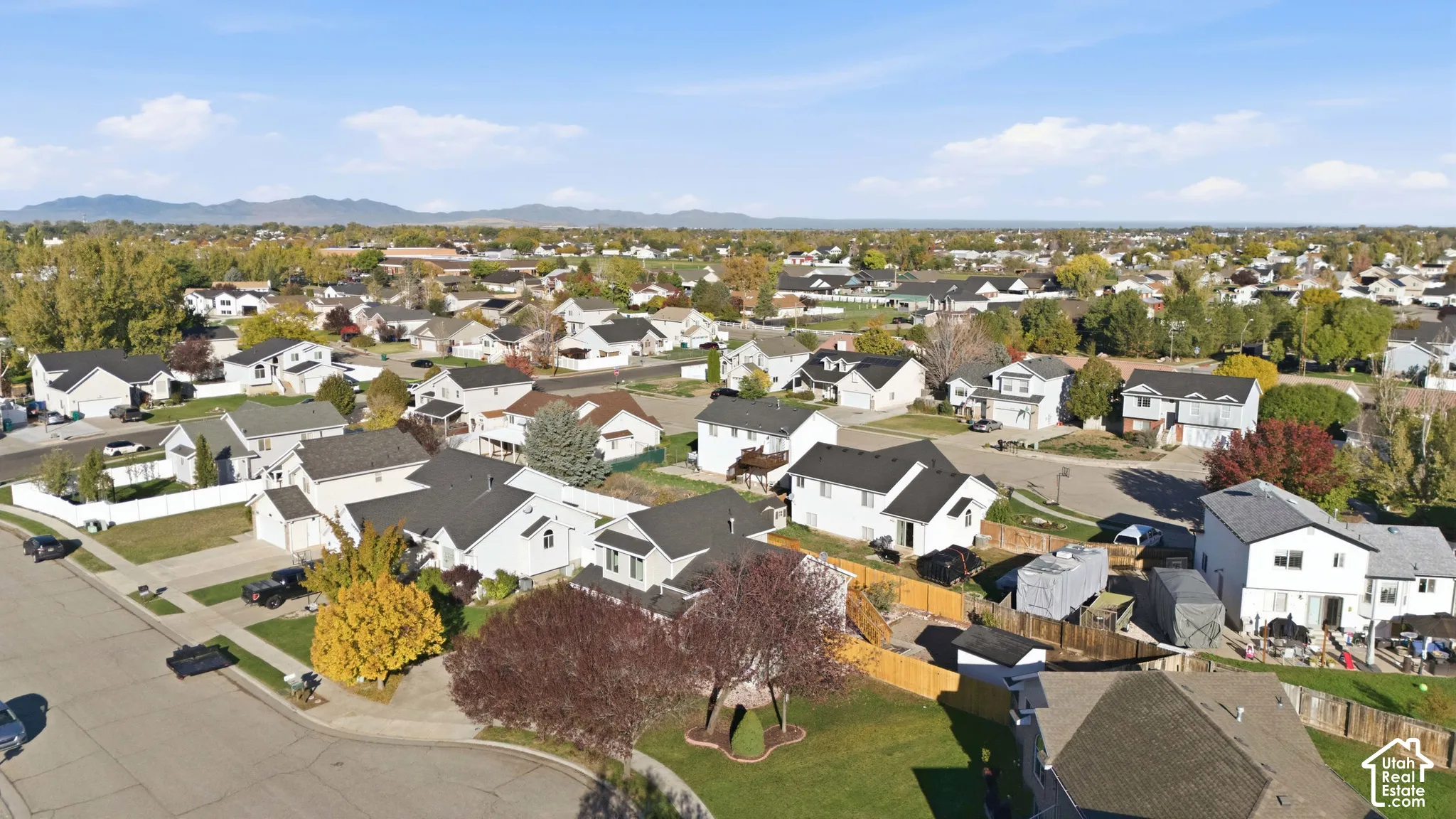 Aerial perspective of a suburban neighborhood featuring paved streets, established deciduous trees, multi-roofline residential architecture, and a prominent mountain range backdrop