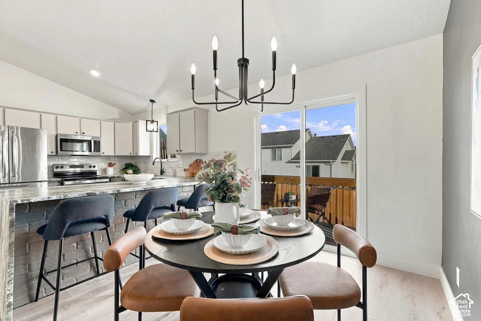 Kitchen featuring vaulted ceilings, a brick-front breakfast bar, matte black chandelier, and sliding glass doors leading to an outdoor deck