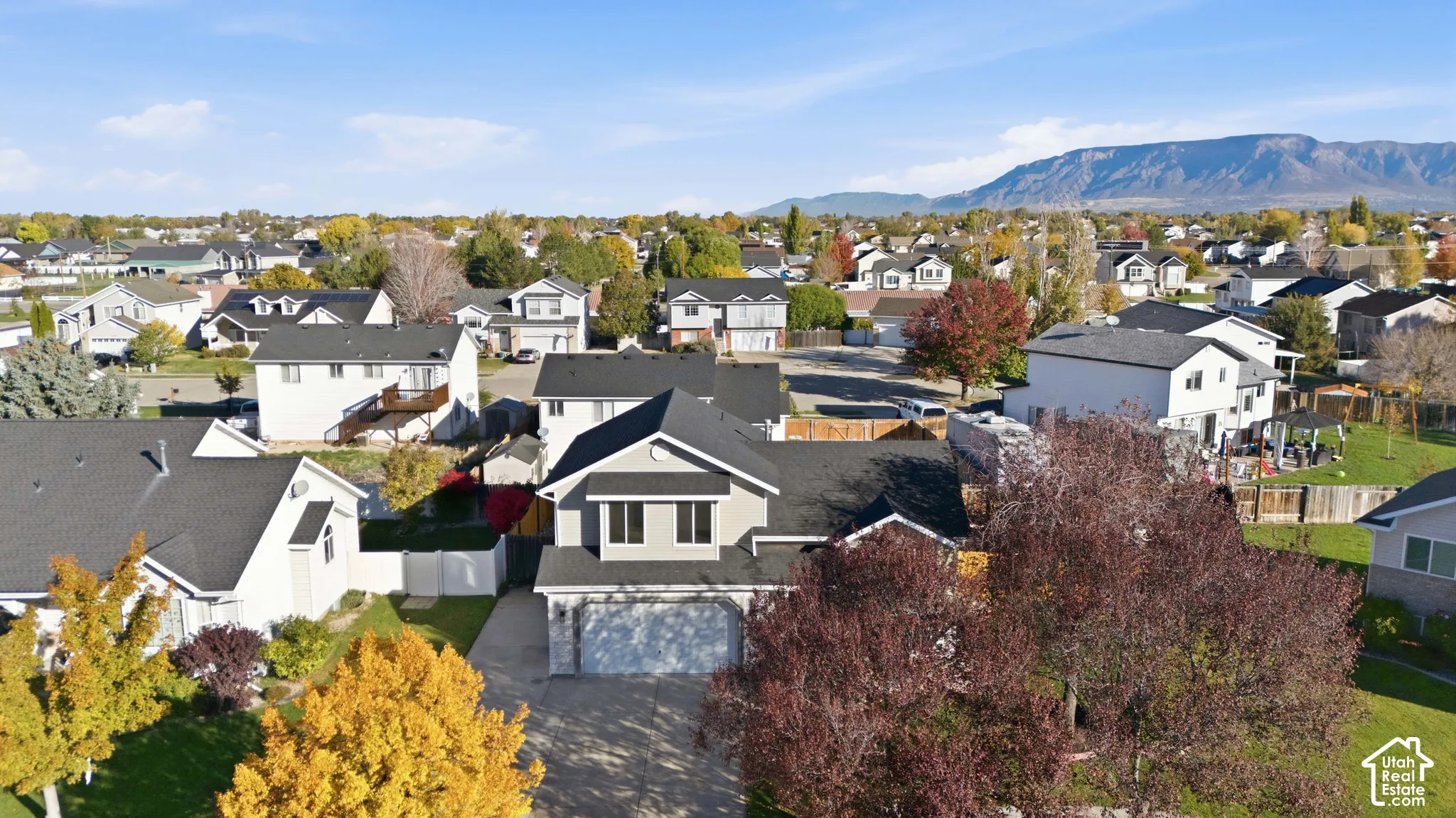 Aerial perspective of a multi-level residence featuring a multi-pitched roof, attached multi-car garage, and concrete driveway, situated within a neighborhood landscape framed by a mountain backdrop