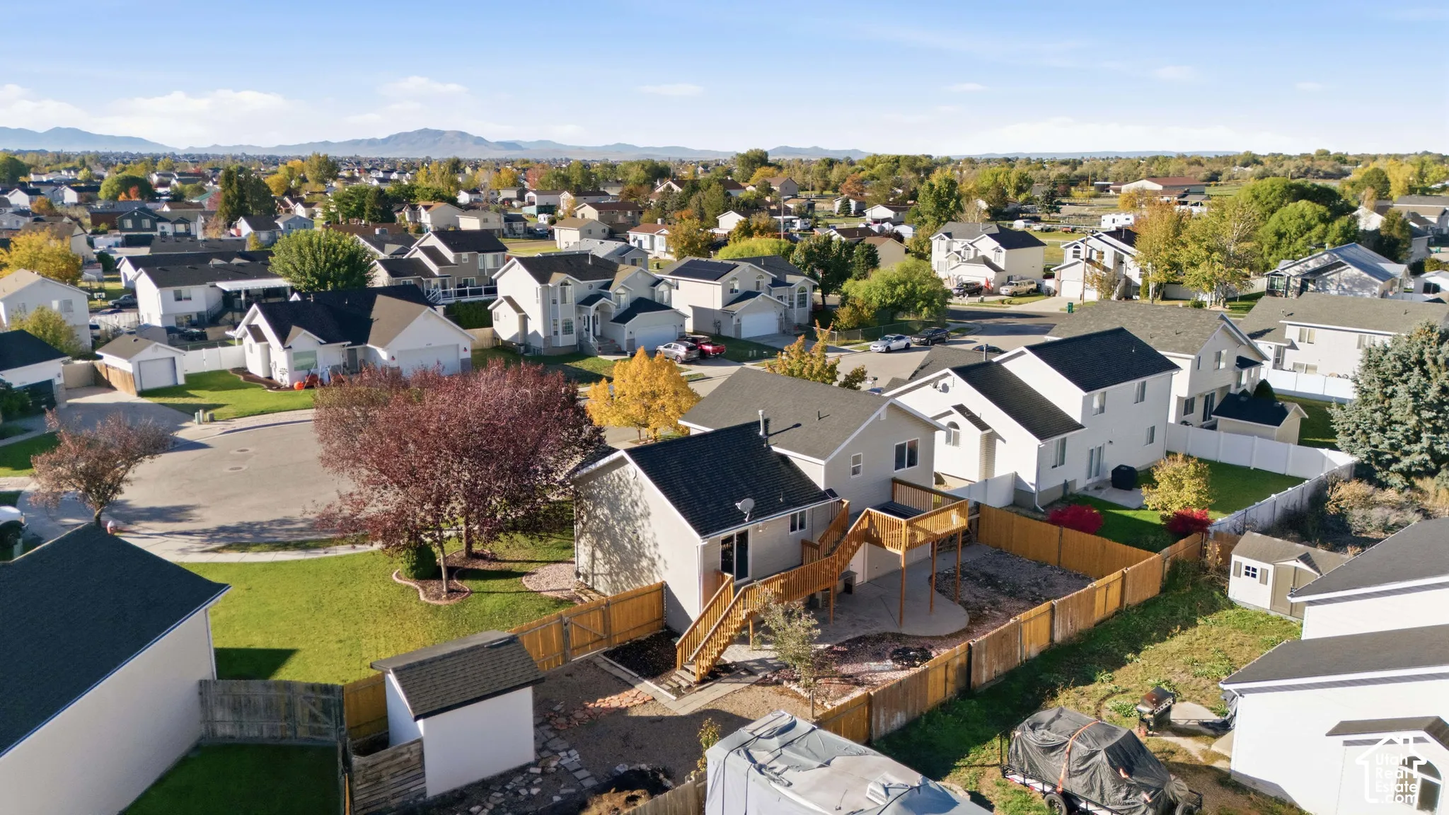 Aerial perspective of property featuring a wood deck, a fenced backyard, and a storage structure, set against a mountain backdrop